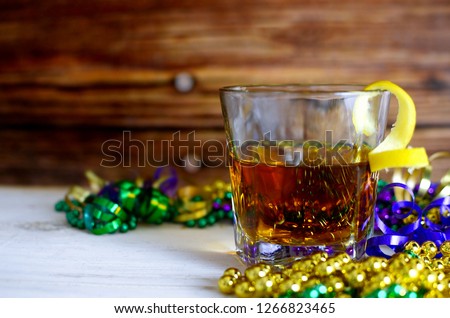 A sazerac cocktail with a lemon twist in a rocks glass on a wooden table. Mardi gras decorations around. Wooden background.