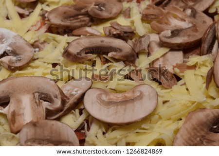 Fresh uncooked homemade pizza heavily topped wiht grated cheddar cheese and sliced mushrooms 