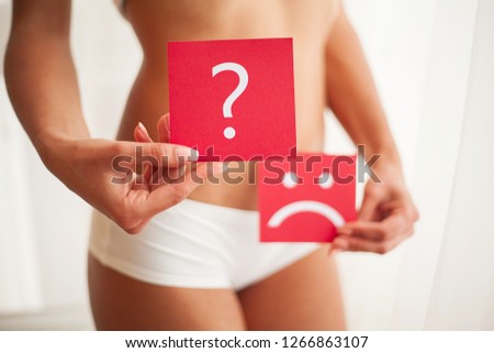 Woman Health Problem. Closeup Of Female With Fit Slim Body Holding Cards With Sad Smiley Face and Question Mark Near Her Stomach. Digestive Disorders, Period Pain, Health Issues Concept.