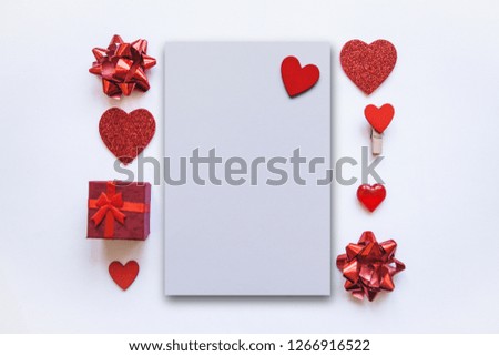 Flat lay various holiday objects including a box with a gift, heart and other things for Valentine's Day and Women's Day. In the middle is a white sheet of paper with a heart for text.