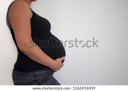 Close up of unidentifiable single pretty pregnant woman in black tshirt holding belly in front of white background with copy space.