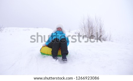 Happy girl slides through snow on sled, beautiful young woman slides down slide in snow on an inflatable snow tube and waves her hand. girl playing in park for Christmas holidays in winter