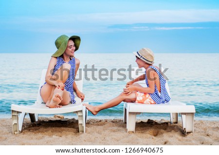 A boy and a girl are having fun talking while sitting on a deck chair by the sea. Brother and sister on vacation. Teenage relationship