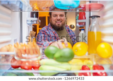 Man looking for something to eat at night while standing in front of opened fridge. Unhealthy eating concept. Picture taken from the inside of fridge.