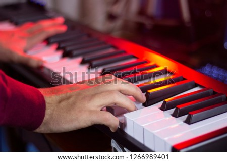 hands of pianist playing midi keyboard, illuminated with colorful lights in the recording studio, close-up