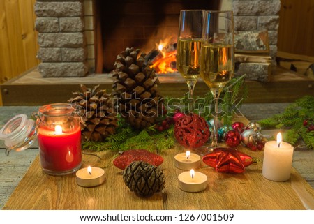 Two shampagne glasses, christmas decorations and candles against cozy firepace.