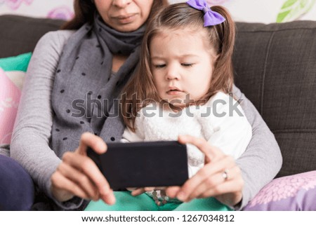Baby girl watching film on internet using smartphone while sitting with parent at home