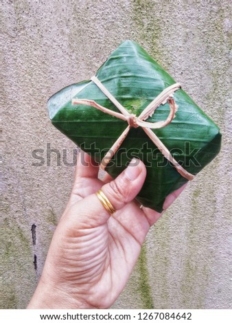 Environment friendly concept of woman hand holding food packaging made from real banana leaves with ribbon & rope from tree bark on grunge & dirty cement background texture. Global warming theme