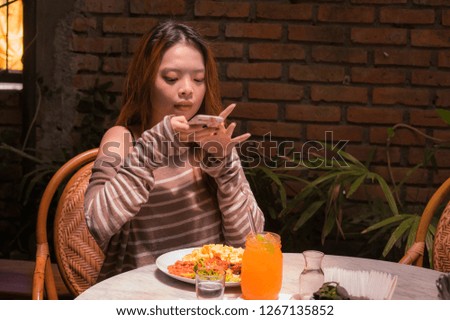lifestyle portrait of young pretty and happy Asian Korean student girl sitting at sweet coffee shop taking photo of her meal with mobile phone camera in internet social media food blogger concept