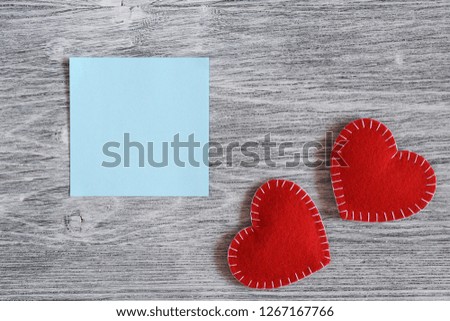 Valentine day picture. Two red felt handmade hearts  and a white paper sheet on a gray wooden background. Top view. Flat lay