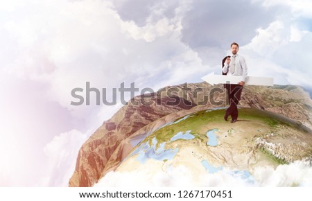 Young successful businessman in suit keeping big white arrow and pointing away while standing on Earth glove and cloudy sky on background. Elements of this image are furnished by NASA