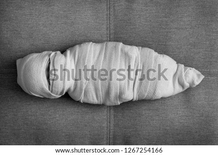 The doll the baby is wound with fabric. The body of the child is shrouded in a shroud. The concept the Muslim dead man. A mummy on a dark background Royalty-Free Stock Photo #1267254166