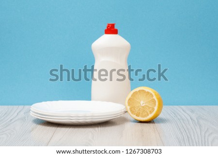 Plastic bottle of dishwashing liquid, clean plates and lemon on wooden boards and blue background. Washing and cleaning concept.