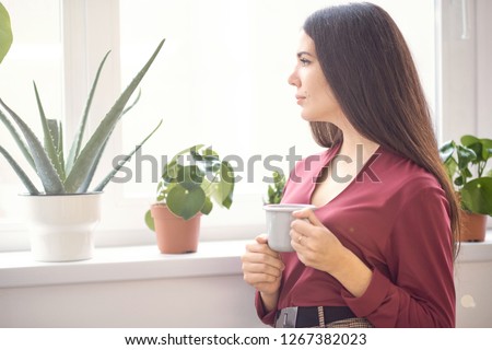 Young attractive girl sitting alone near big window in coffee shop during free time and working