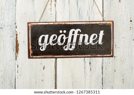 Old metal sign in front of a white wooden wall - German word for Open - geoeffnet