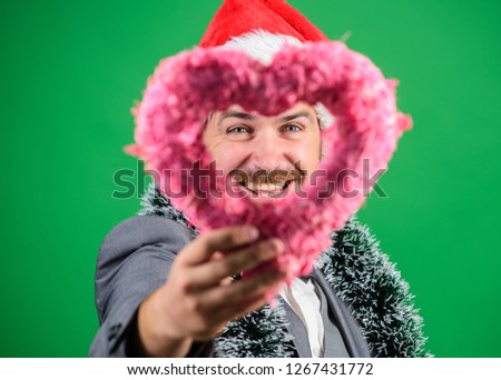 Merry christmas and happy new year. Hipster hold heart symbol of love. Bring love to family holiday. Man in love happy wear santa hat celebrate christmas green background. Spread love around.