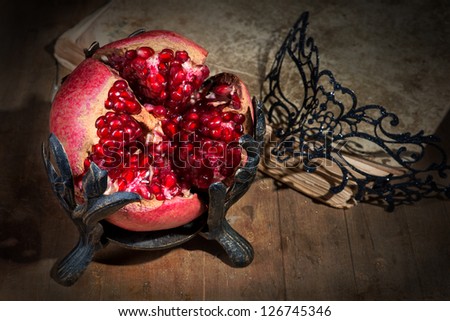 Vintage still life with pomegranate, lacy mask and ancient book on wooden table