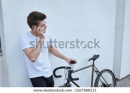 Young hipster style man posing with bicycle on the street sport style picture handsome guy white wall