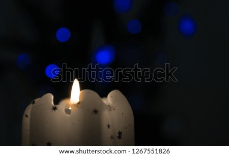Glowing candle in the dark with blue bokeh light in the background. Burning flame of a white candle. Copy text space.