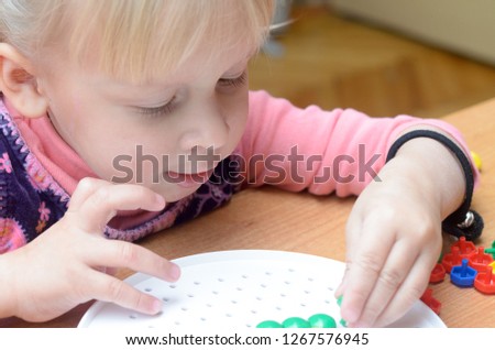 A little girl collects a colorful mosaic at the table