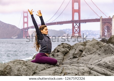 Early 20s women working on self-care by doing yoga on the beach just outside of San Francisco with the Golden Gate Bridge in the background