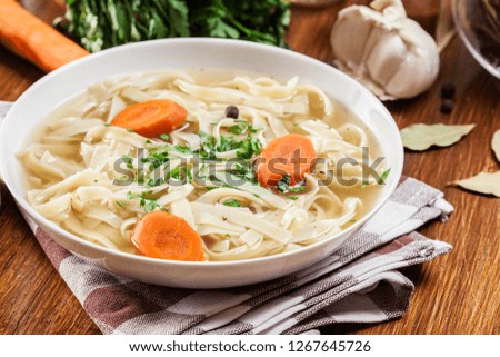 Tasty meat broth with noodles, carror and parsley in a plate