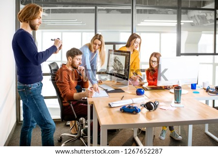 Group of young creative coworkers designing a car model at the working place with computers in the modern office interior