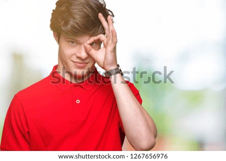 Young handsome man wearing red t-shirt over isolated background doing ok gesture with hand smiling, eye looking through fingers with happy face.