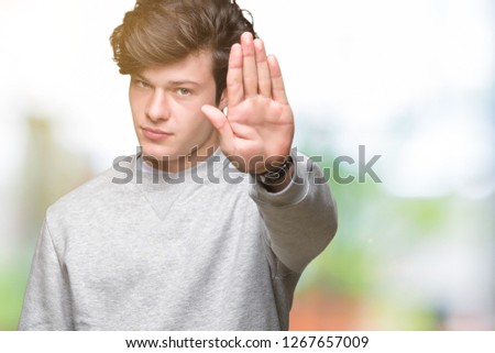 Young handsome sporty man wearing sweatshirt over isolated background doing stop sing with palm of the hand. Warning expression with negative and serious gesture on the face.