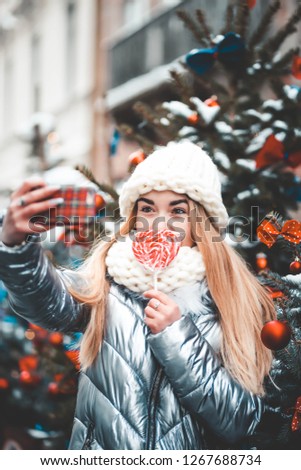 Beauty teen with lollipop making selfie on the background of the Christmas tree