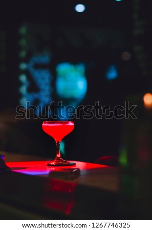 Red Cocktail drink-beverage on  a bar.  Selective focus on the foreground glass,night background . Blurred people in the background.  Trendy black stylish  edit. Copy paste space for design concept