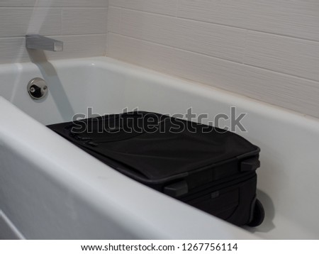 A black suitcase placed flat in a white hotel bathtub by a savvy business traveler. Bed bugs are unable to climb the smooth walls of the tub