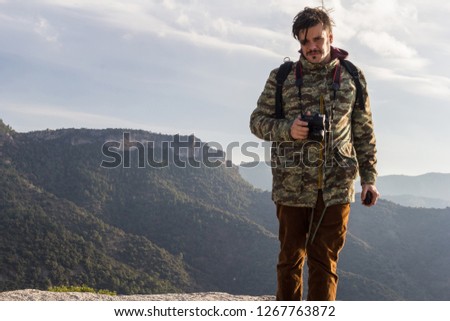 Photographer taking photo in the middle of the wild nature of the top of the mountain with clothes mussed in the cold	
