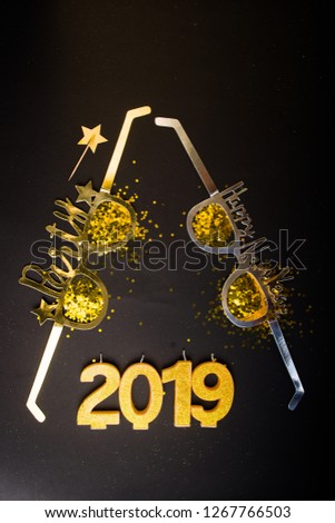 New Years Eve celebration background , 2019 number made with golden glitter candles and decorations, flatlay over a black board, luxury  holiday concept, with funny party glasses.
