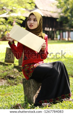Cute girl holding empty sign. Girl wearing hijab. Girl in traditional Malay attire "Baju kurung". Malay traditional concept photo.
