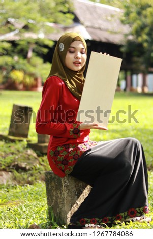 Cute girl holding empty sign. Girl wearing hijab. Girl in traditional Malay attire "Baju kurung". Malay traditional concept photo.