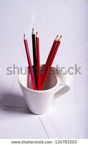 black and red pencils stand in a white cup