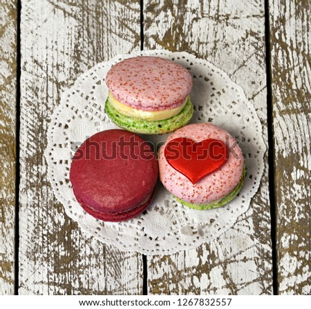 Top view of three delicious macarons and love heart symbol on napkin on wooden table. Romantic vintage valentine’s day and wedding background