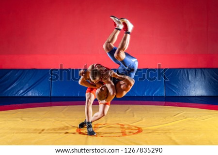The concept of fair wrestling. Two young men in blue and red wrestling tights are wrestlng and making a suplex wrestling on a yellow wrestling carpet in the gym