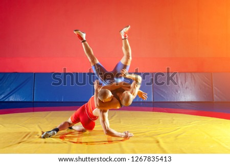 Two strong wrestlers in blue and red wrestling tights are wrestlng and making a suplex wrestling on a yellow wrestling carpet in the gym. Young man doing grapple.
