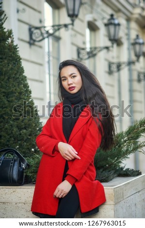Portrait of a young beautiful fashionable woman in a red coat . Model posing on a city street