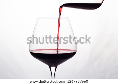 red wine is poured into a wine glass on a white background
