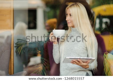 Reading Concept. Young blond Woman using Tablet and Drinking Coffee. Relaxing in Cozy cafe, Sit on the Chair