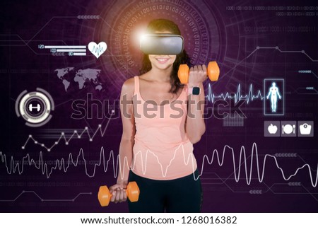 Picture of happy woman wearing a virtual reality glasses while exercising with dumbbells