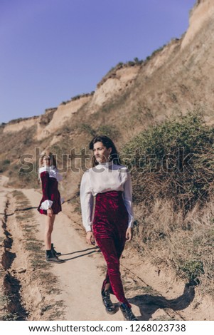 two girls on the road by the cliff, blonde and brunette in burgundy, fashion girls in nature
