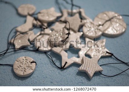 Small ornament pendant star shape figures, made of self drying white clay and shining glitter. Shallow depth of focus, bokeh effect on blue background. Christmas and New year decoration, jewel gift.