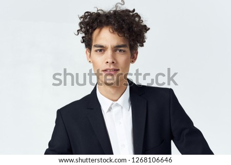 curly guy in a suit on a light background and earrings in his ears                            