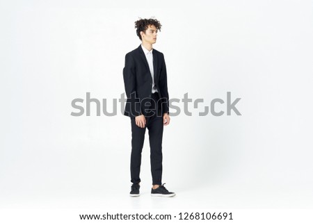 a young guy in catkins and with curly hair is standing in full growth in a classic suit on a light background                        