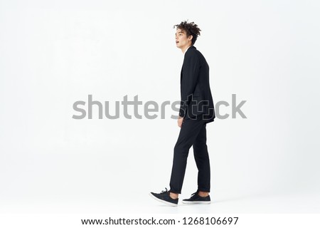 Business man with curly hair and in a classic suit in full growth on a light background, side view      
