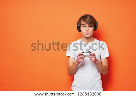 Gamer in headphones and with a joystick in his hands on an orange background                       